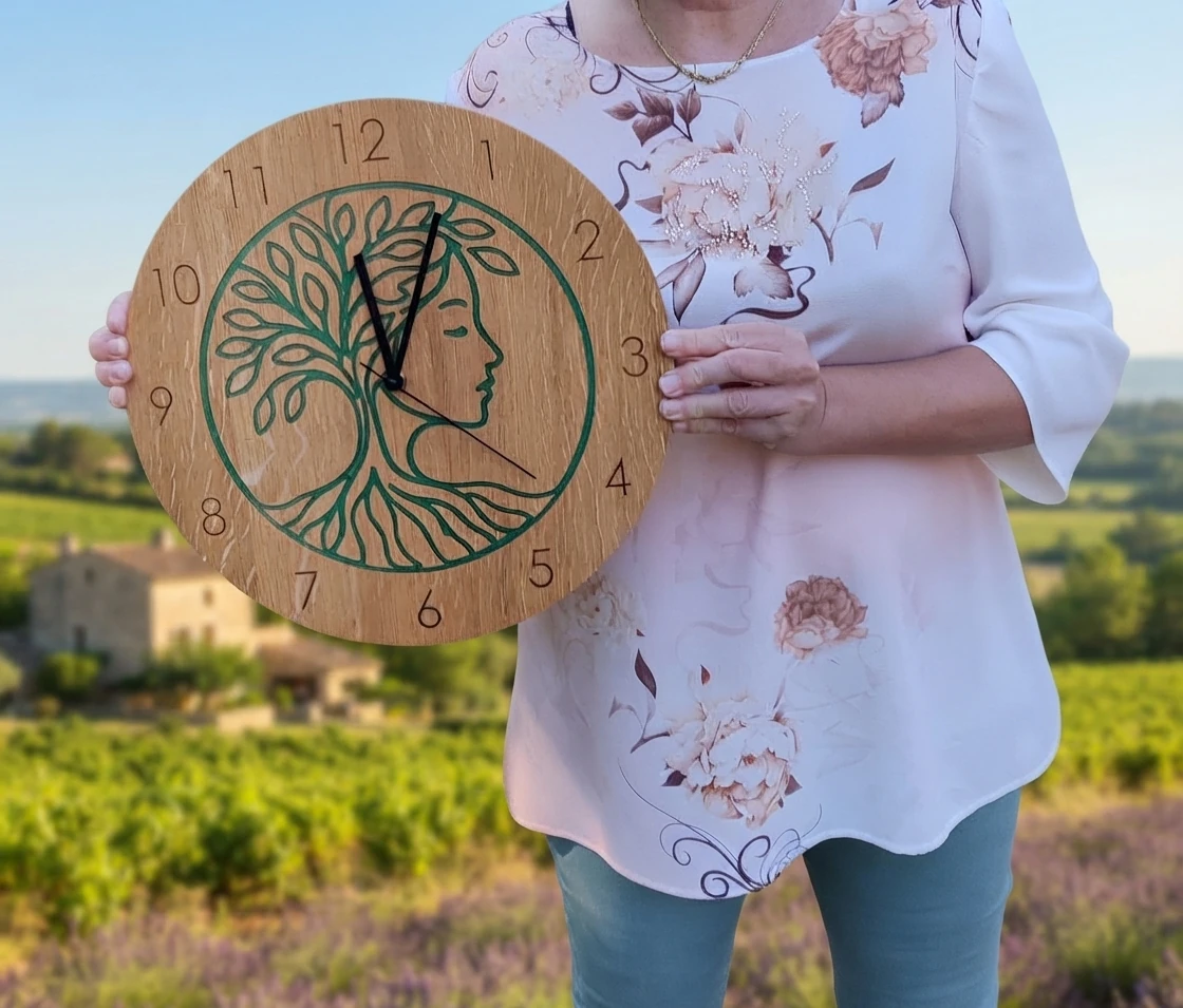 Horloge arbre de vie visage en chêne tenue à la main, pour apprécier ses dimensions